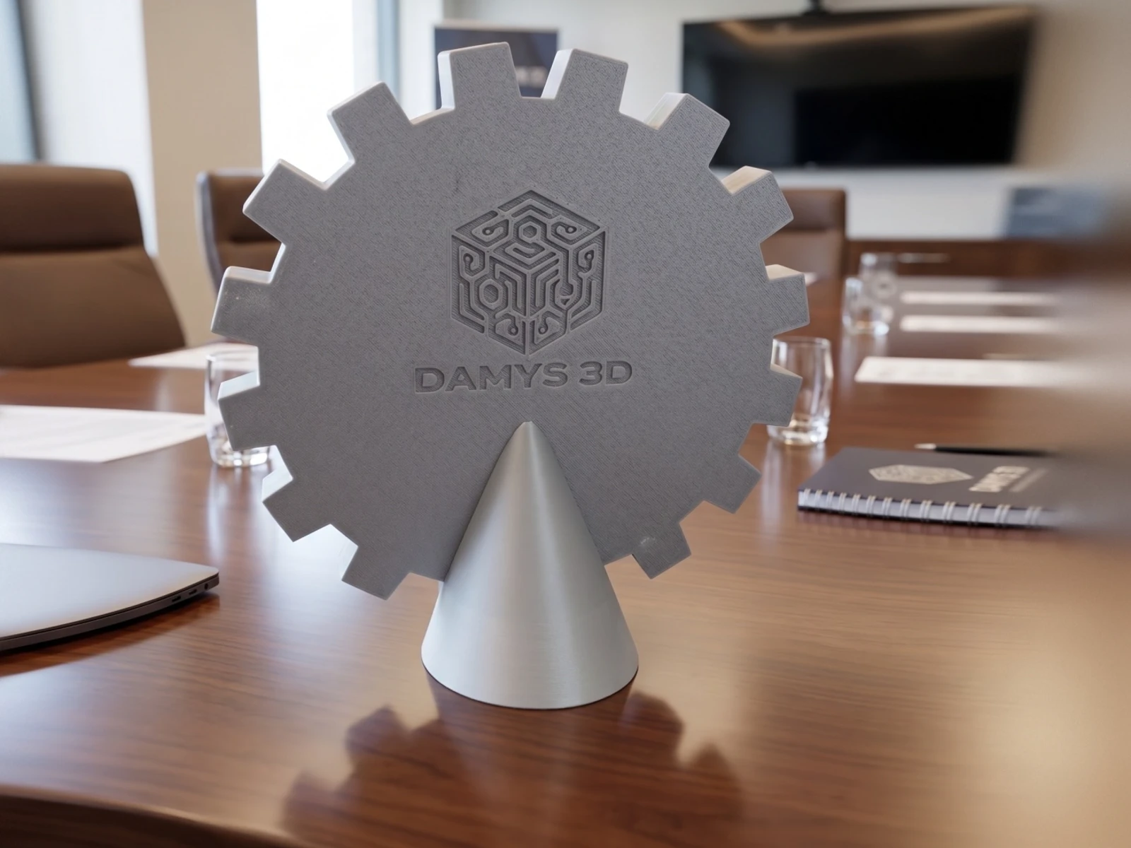 Reverso del logo M&V impreso en 3D con la firma Damys 3D grabada y base cónica autoportante